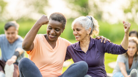 Two senior women at outdoor exercise class smiling and flexing.