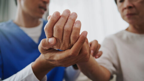 Physical therapist examining a mature woman’s hand during therapy.